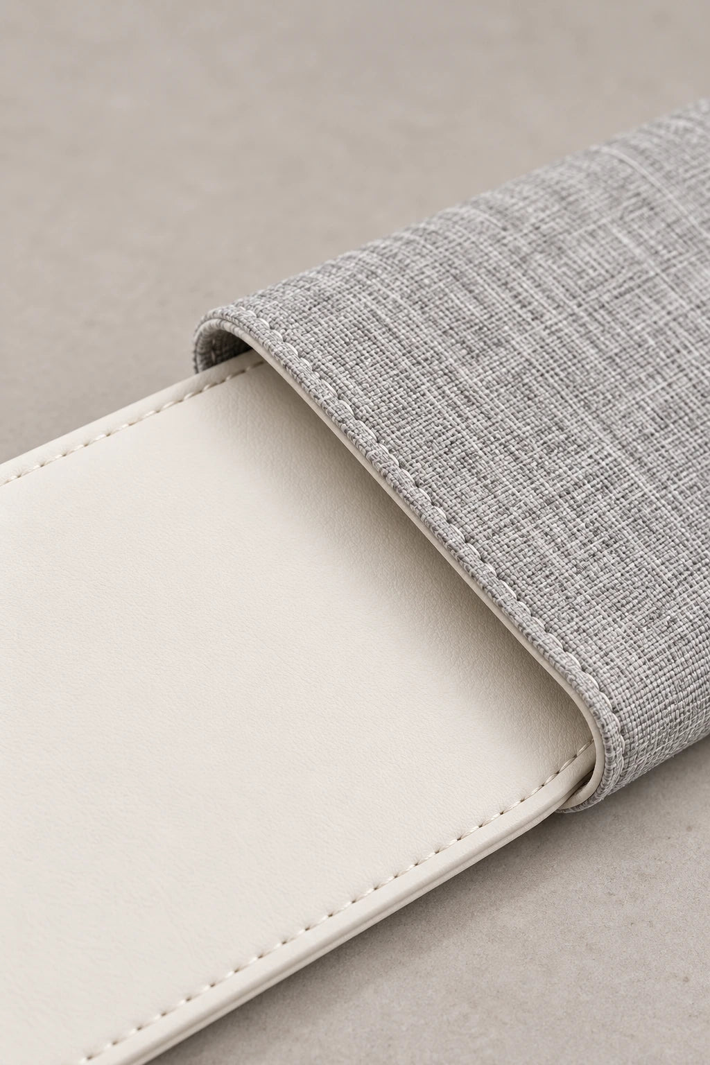 Detail of white vegan leather, stitched piping and gray fabric lining on a folding laptop sleeve.